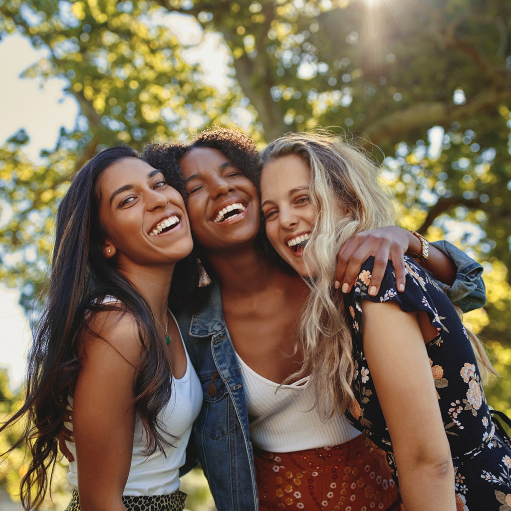Portrait of a happy multiethnic group of smiling female friends - women laughing and having fun in the park on a sunny day